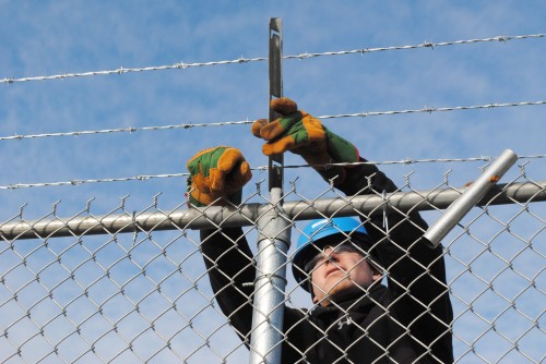 worker installs barbed wire onto a chain link fence