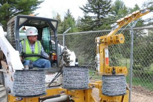 worker loads barbed wire onto a barbed wire dispenser attached to a skid steer